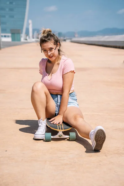 Ritratto giovane donna bionda con skateboard e occhiali — Foto Stock