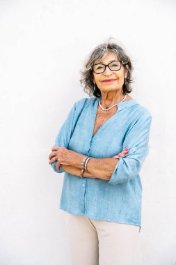 Kıdemli kadın gülümsüyor, özgüvenini dile getiriyor ve beyaz bir arka plana karşı olumlu bir tutum sergiliyor.