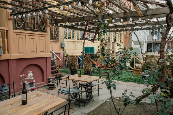 Bir yaz kafesinin verandasında yakınlarda büyüyen bitkilerin yeşilliklerinde masalar vardı.