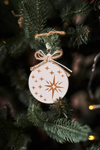 Yeşil bir noel ağacında asılı duran altın yıldızlı beyaz ahşap top ve tuval halat                               