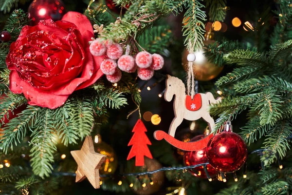 Christmas decorations on the tree: rose flower, snow-covered berries, wooden star, red wooden tree, wooden horse and red ball