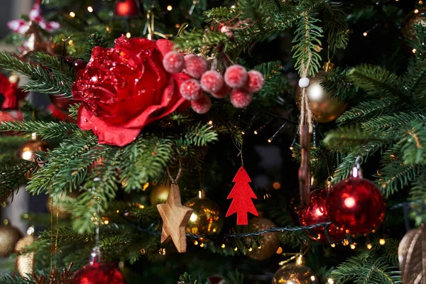 Christmas tree decorations in the form of a beautiful red rose, a wooden star and a red wooden Christmas tree and red and other balls hang on the Christmas tree