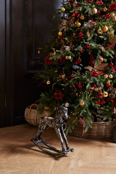 Ağacın altındaki siyah tahta at. Kırmızı ve altın toplarla süslenmiş sepetin içinde.                                 