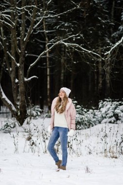 Beyaz tüylü eldivenler içinde güzel bir kız, bir şapka ve açık renk elbiseler kışın parkta duruyor.