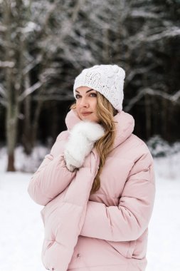 Genç ve güzel bir kadın kendini karlı bir parkta kalın bir cekete sarar.
