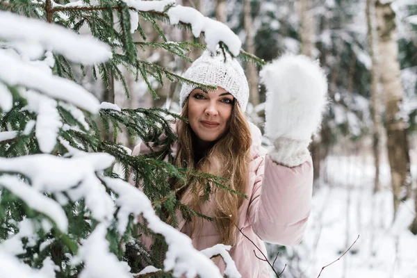 Uzun saçlı güzel bir kız köknar ağacının kar kaplı dallarının arkasından dışarı bakıyor.