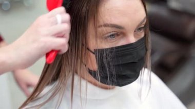 Siyah koruyucu maskeli, ıslak saçlarını fırçayla tarayan bir kadının yakın çekimi..