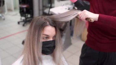 Siyah maskeli bir kız saçını yuvarlak bir fırçadan çekerek kurutuyor.