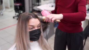 Güzellik salonunda, kuaförde, saç kurutma makinesi ve saç fırçasıyla sarışın kızın saçını kurutuyor.