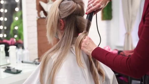 理发师的双手用矫直机捏住一缕头发 然后伸展 拧在镜子前卷曲着女孩金色长发的锁 — 图库视频影像