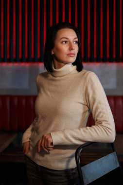 Zarif hatlara sahip güzel bir kız ve omuz hizasında koyu renk saçlar açık renk bir süveter içinde boğazı yana bakan bir kız.                               