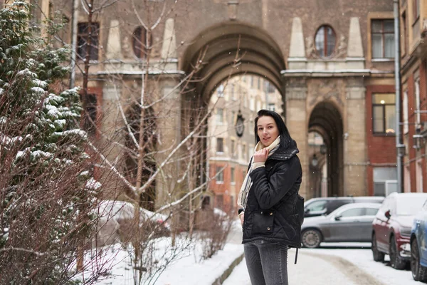 Güzel esmer kız kışın yüksek kemeri olan eski güzel bir binanın avlusunda.                               