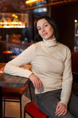 Güzel esmer kız bir kafede yüksek bir masada oturuyor.                               