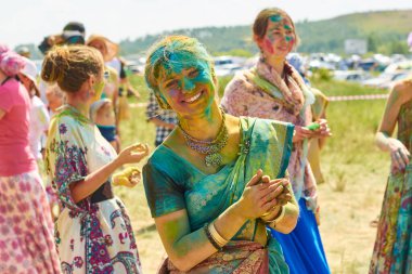 Rusya, Arkaim 2015.06.21: Yüzü ve vücudu boyayla lekelenmiş güzel bir kız, diğer insanların arka planında Holi renk festivalinde geleneksel Hint elbisesi giyiyor.