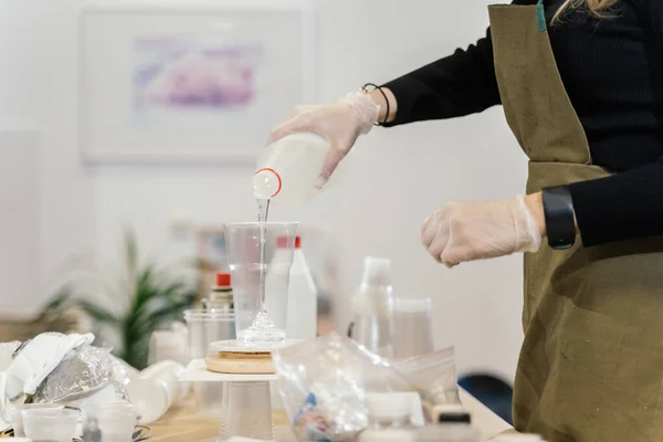 Önlüklü ve şeffaf eldivenli bir kız şeffaf plastik bir bardağa temiz sıvı döker.