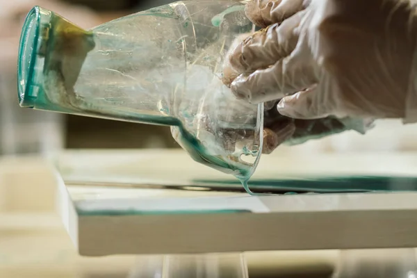 Şeffaf eldivenli eller buruşmuş şeffaf plastik bardaktan pürüzsüz beyaz bir yüzeye renkli sıvı döker.