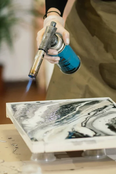 Eldivenli bir kızın elindeki özel bir gaz ocağı resimdeki epoksi reçineyi eritip güzel bir oyun ve sıvı mermer etkisi yaratır.