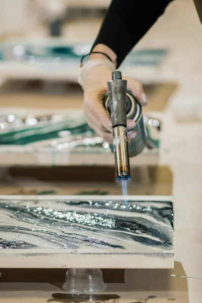 Eldiven içindeki bir kadın el yapımı bir gaz ocağı tutuyor ve reçine sanatı tekniğini kullanarak güzel bir tablo yaratıyor.