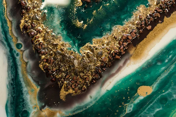 Parlak yeşil, turkuaz ve altın reçine dereleri üzerinde bronz taşlar ve altın tozları, bulanık dalgalar. Soyut bir arkaplanda değerli taşların kesiminin taklidi
