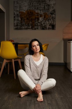 Açık renk elbiseli güzel, genç esmer kadın mutfak zemininde oturur, bacak bacak bacak üstüne atar.                               