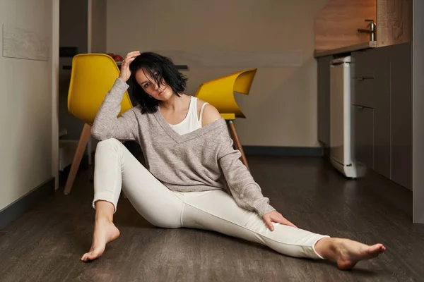 Açık renk elbiseli güzel, genç esmer kadın yere oturur, bir bacağını uzatır, dirseğini diğerinin dizine yaslar ve eliyle başını tutar.                               