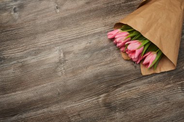 Bir buket narin pembe lalenin içinde buruşmuş kağıt, ahşap bir masanın üzerinde yatıyor.