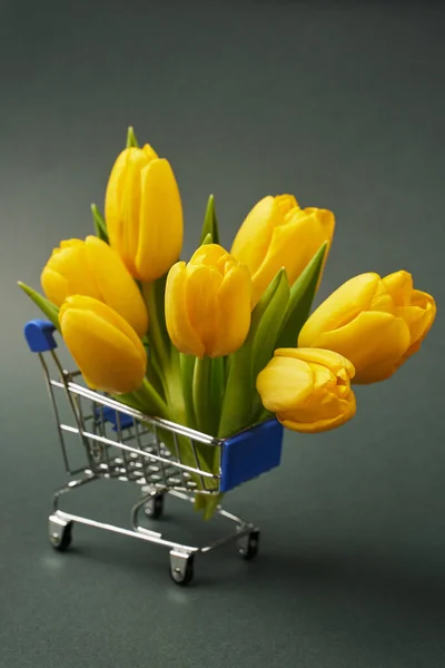 Gri arkaplanda dikey fotoğraf süpermarket arabasında güzel sarı laleler