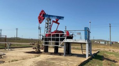 Endüstriyel petrol pompası, petrol sahasında sondaj kulesiyle ham petrol için çalışıyor ve pompalıyor. Mavi gökyüzüne kafa sallayan eşek pompamız güneşli yaz mevsiminde güneşin üzerinden pompalanıyor.