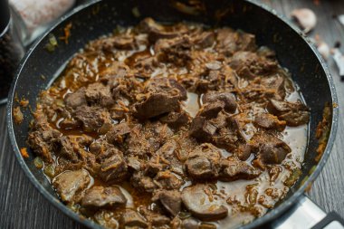 Kızarmış tavuk ciğeri, soğan ve havuç. Siyah bir tavada yakın plan.