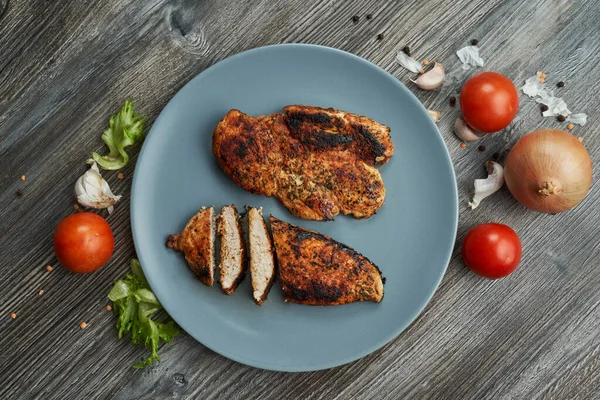 Tabakta iki kızarmış tavuk göğsü. Taze sebzeler yakında.