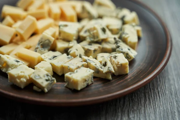 Üzerinde iki çeşit peynir bulunan kahverengi bir tabak, ön planda mavi dor mavi peyniri, küp şeklinde kesilmiş. seçici odak