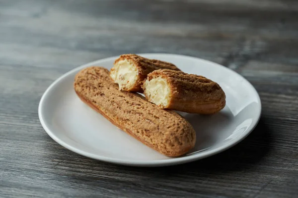 İçinde krema olan iki eklem beyaz bir tabakta. Biri ikiye bölünür ve ikincisi yalan söyler. Tabak gri ahşap bir masada duruyor.