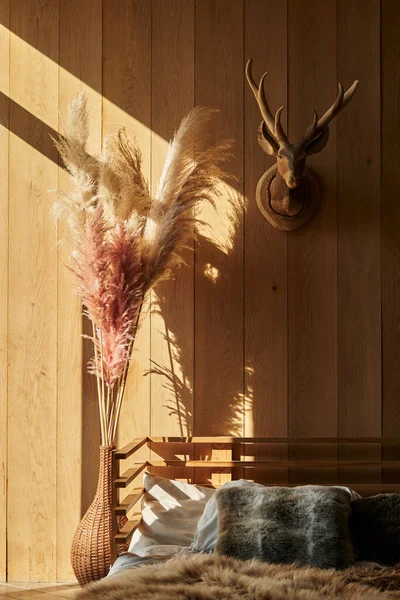 İskandinav tarzı yatak odasında bir buket uzun pampa otu. Yere yatın. Ahşap iç döşeme, duvarlar ve yatak.