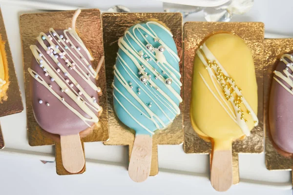 Sarı, mavi ve çikolata renkli buzlu şeker. Gümüş ve altın kaplamalı buzlu kekler.