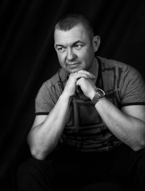 Stüdyoda bir adamın siyah beyaz portresi. Elleri çenesinin altında, yan tarafına bakıyor.