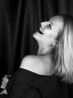 Stüdyoda çıplak omuzlu, siyah şortlu, hassas ve şehvetli sarışın bir kadının siyah beyaz portresi yarım yamalak duruyor. Kafasını geriye attı ve gülüyor.
