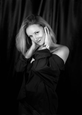 Siyah-beyaz bir portre. Stüdyoda siyah şortlu, boynu ve yüzü önünde eğik duran, çıplak omuzlu, hassas ve şehvetli sarışın bir kadın.