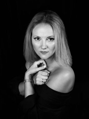 Stüdyodaki hassas ve şehvetli sarışın bir kadının siyah ve beyaz portresi. Çıplak omuzlu bir sandalyede oturuyor. Yukarıdan çekilmiş, bakışları kameraya çevrilmiş, elleri göğsünde çapraz.