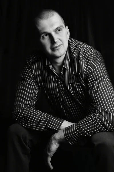 Black and white portrait of a man in the studio, sitting with his hands cross,ooking on the side up