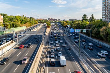 Madrid, İspanya. 9 Ekim 2025. Madrid 'in doğusundaki M30 otoyolunda yoğun trafik görüntüsü, hafta içi öğleden sonra dağınık bulutlar ve şehir binalarıyla yakalandı..