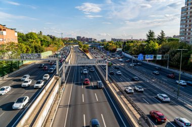 Madrid, İspanya. 9 Ekim 2025. Madrid 'in doğusundaki M30 otoyolunda yoğun trafik görüntüsü, hafta içi öğleden sonra dağınık bulutlar ve şehir binalarıyla yakalandı..