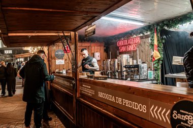 11 Aralık 2025. Madrid, İspanya. San Gines çikolata tezgahı Plaza de Espana 'daki Noel pazarında faaliyet gösteriyor ve festival dekorasyonları ve kış kalabalığı arasında geleneksel sıcak çikolata sunuyor.
