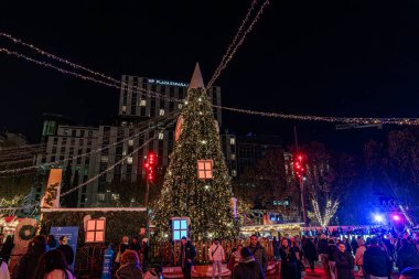 11 Aralık 2025. Madrid, İspanya. Plaza de Espana 'daki Noel pazarında ahşap tezgahlar, şenlikli ışıklar ve insanlar kış tatili boyunca gece boyunca şehir meydanında yürüyüp alışveriş yapıyorlar..