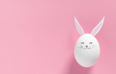 Tavşan kulaklı Paskalya yumurtası ve pembe arka planda fotokopi alanı olan bir yüz. Düz ya da üst görünüm. Minimum konsept. Kavramsal yaratıcı fotoğraf yaklaşıyor. Mutlu Paskalyalar.
