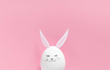 Tavşan kulaklı Paskalya yumurtası ve pembe arka planda fotokopi alanı olan bir yüz. Düz ya da üst görünüm. Minimum konsept. Kavramsal yaratıcı fotoğraf yaklaşıyor. Mutlu Paskalyalar..