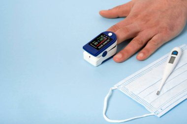 İnsan eli nabız oksimetresi nabız ve oksijen seviyelerini ölçmek için kullanılır. Tıbbi mavi arka planda fotokopi uzayı vardır. Üst Manzara. Tıbbi konsept koruyucu tıbbi maske, elektronik termometre 