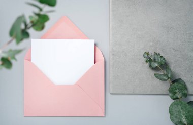 Gerçek fotoğraf. Okaliptüs dallı pembe zarf kare davetiye modeli. Üst görünümü kopyalama alanı, açık gri arkaplan. Markalaşma ve reklam şablonu