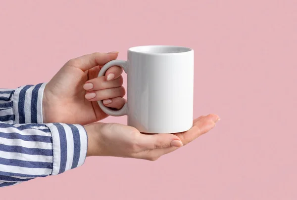 Beyaz kahve fincanı ya da kadın ellerinde kupa. Pembe arka planda fotokopi alanı var. Tasarım, marka ve iş için boş bir şablon. Çizgili tişörtlü kadın günlük tarzında. Gerçek fotoğraf..