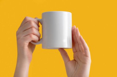 Seramik beyaz kahve fincanı ya da kadınların elinde fotokopi çeken sarı arka planda duran kupa. Tasarım, marka ve iş için boş bir şablon. Sıradan giyinmiş bir kadın. Gerçek fotoğraf..