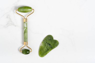 Yüz masajı için Jade Roller. Yeşil gua sha yüz masajı araçları mermer beyaz arka planda fotokopi alanı düz yatıyordu. Yaş, kaldırma ve tonlama tedavisi, akupres.